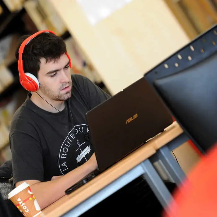 male students with headset working on a laptop in the library of Brunel